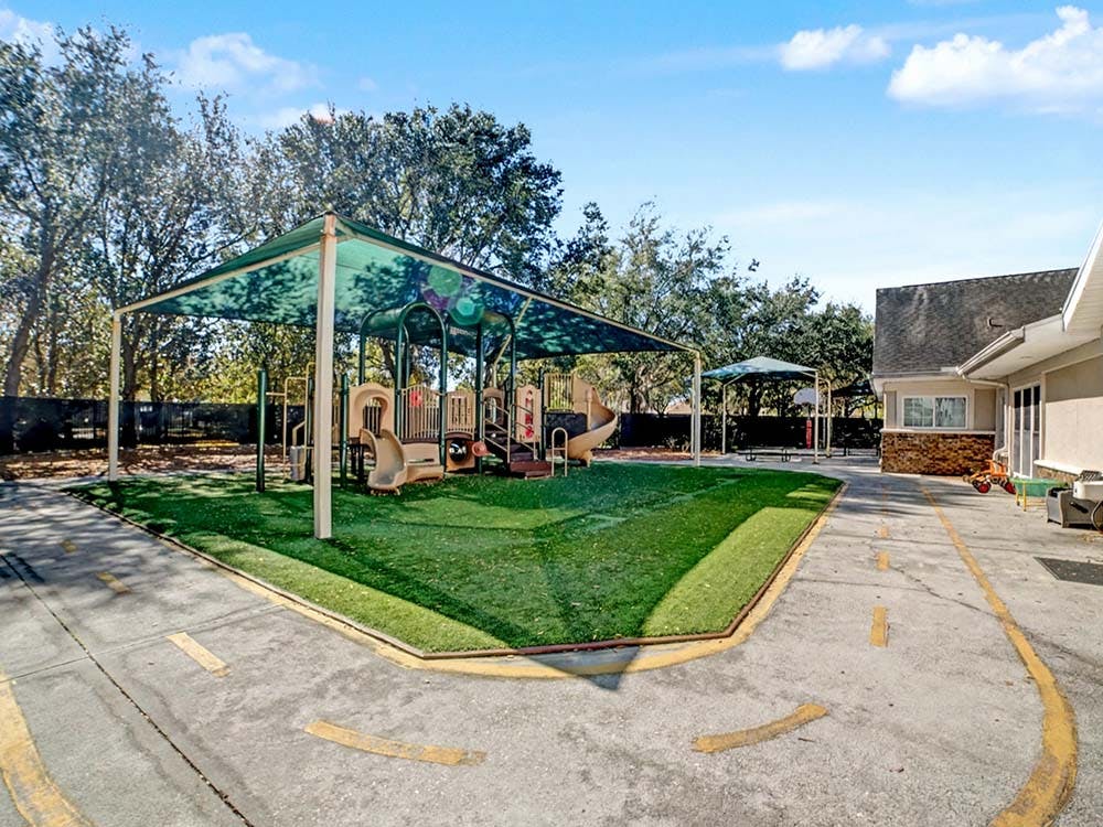 Outdoor playground with artificial turf under a large shade structure