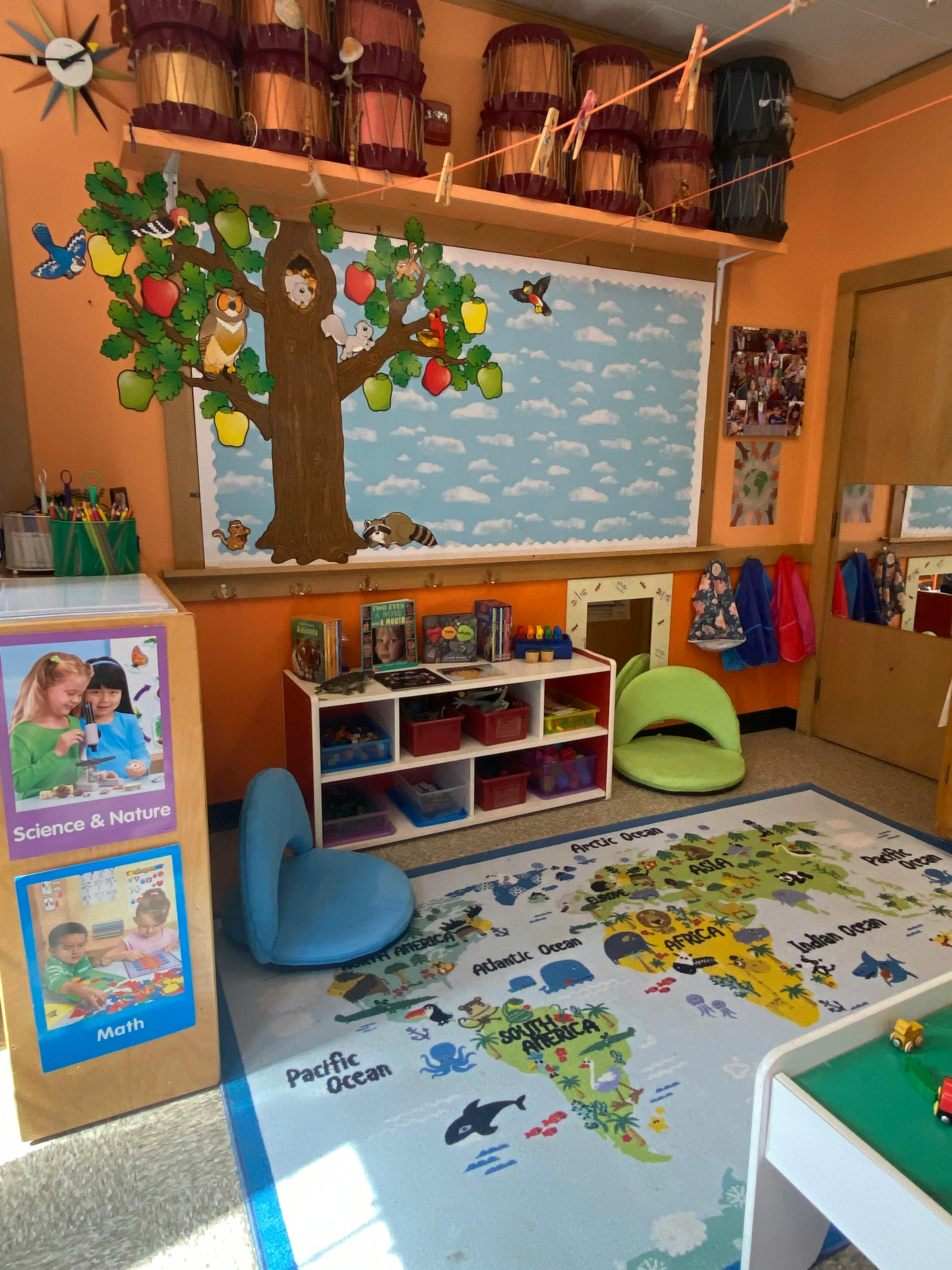 Classroom with a world map rug, shelves, and a tree mural