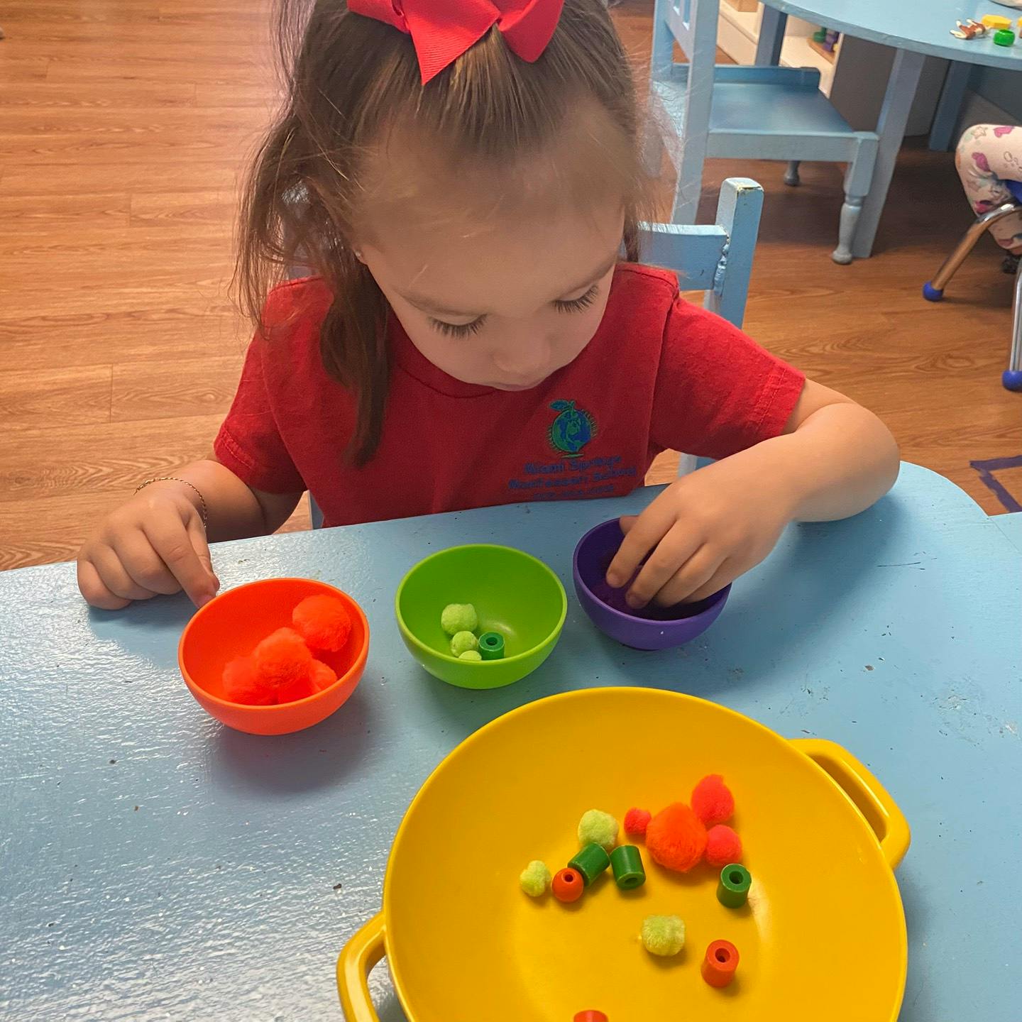 Child sorting small objects into colored bowls at a table