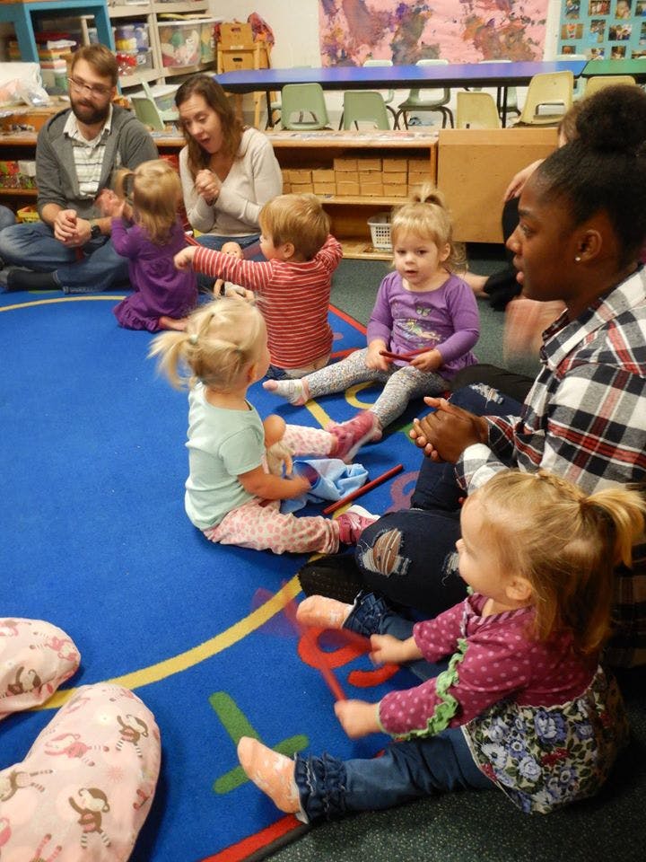 Adults and children sitting on a blue rug in a classroom