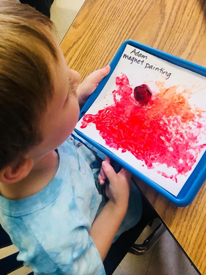 Child looking at a magnet painting with red paint