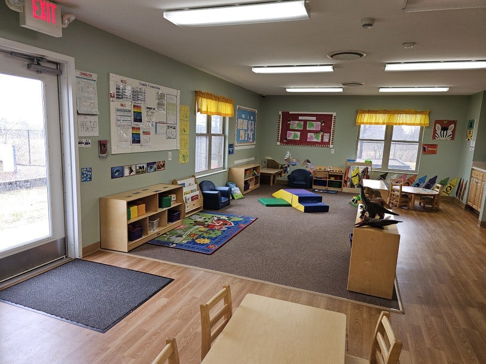 A classroom with small tables and chairs, shelves, and a rug with toys