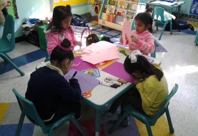Four children doing crafts at a table in a classroom
