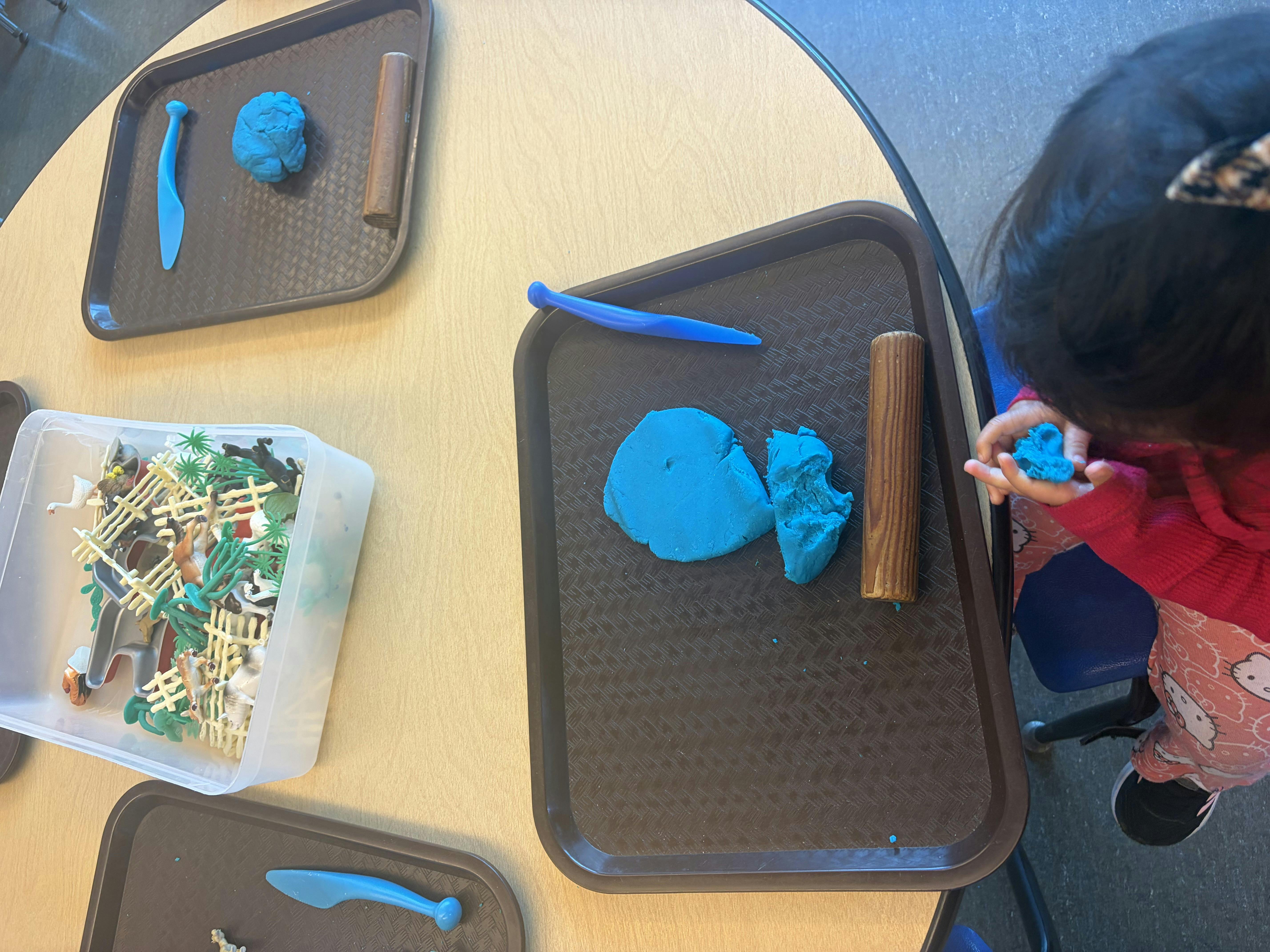Child playing with blue playdough and plastic toys at a table