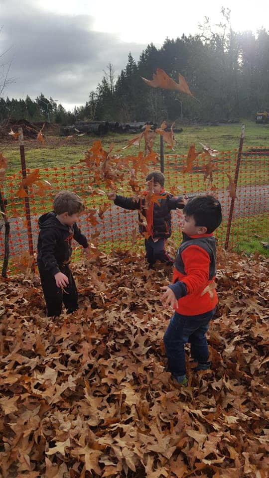 Three children playing in a pile of autumn leaves outdoors