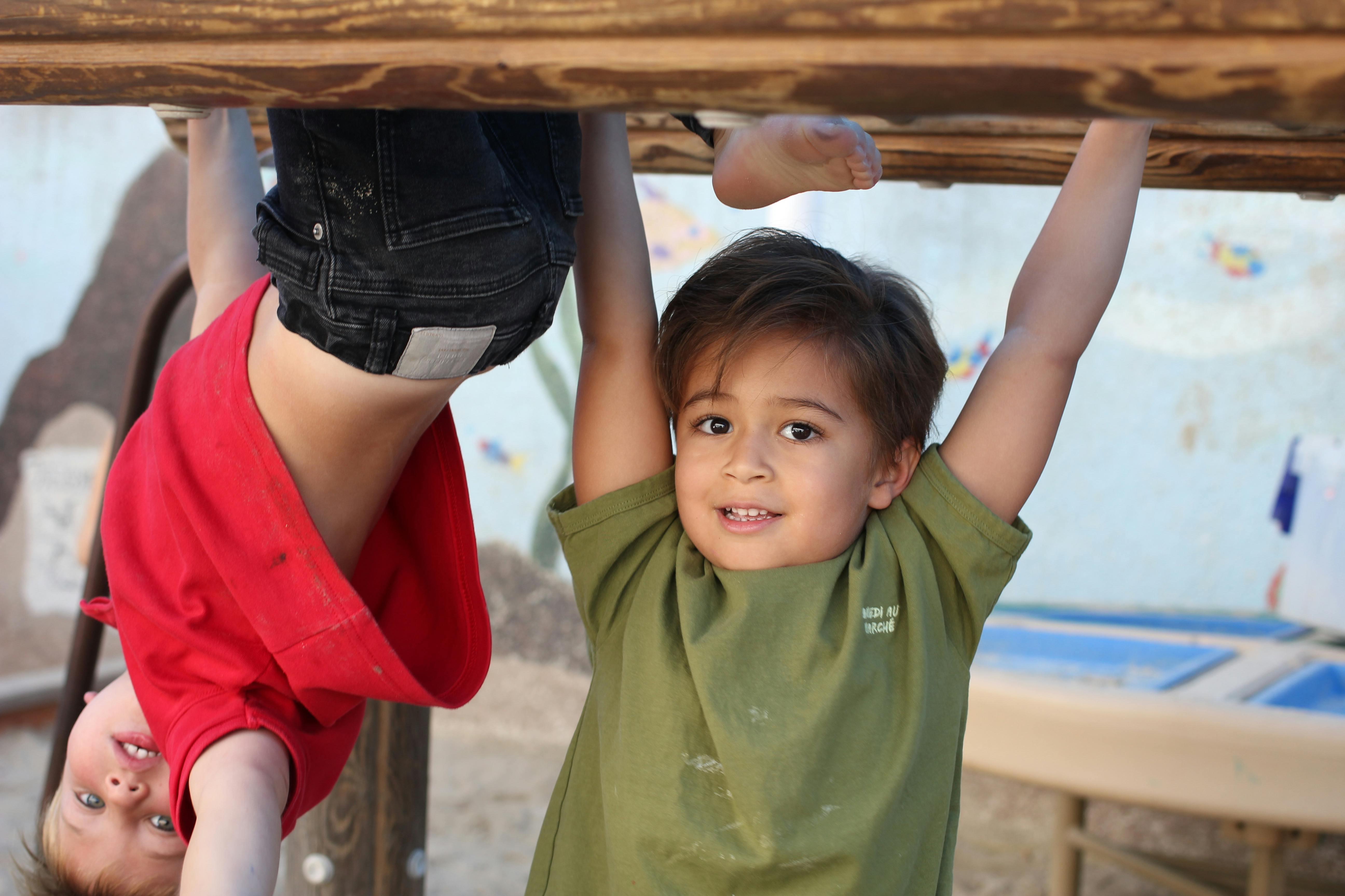 Two children hanging upside down from a wooden beam