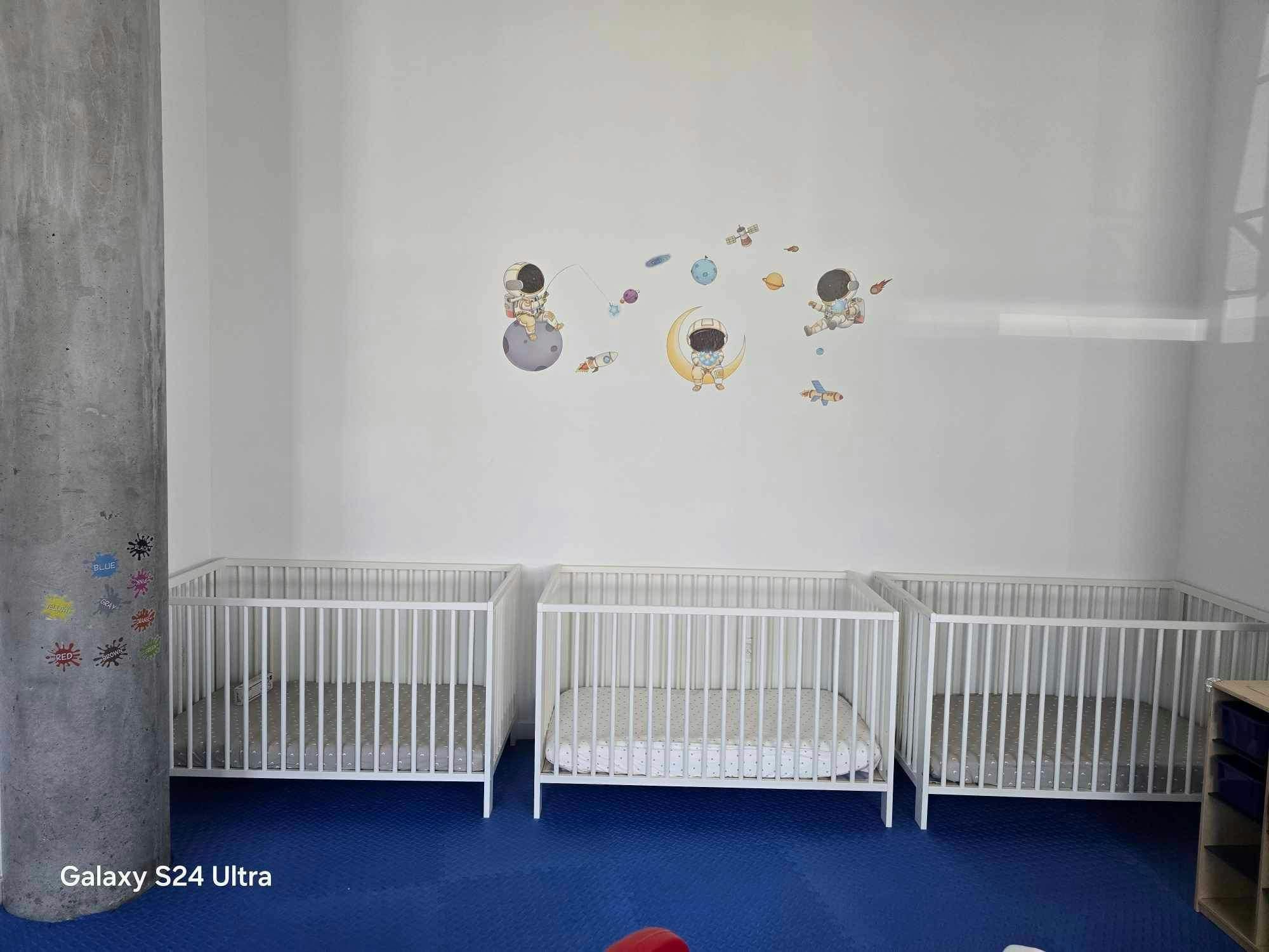 Three white cribs in a room with space-themed wall decals