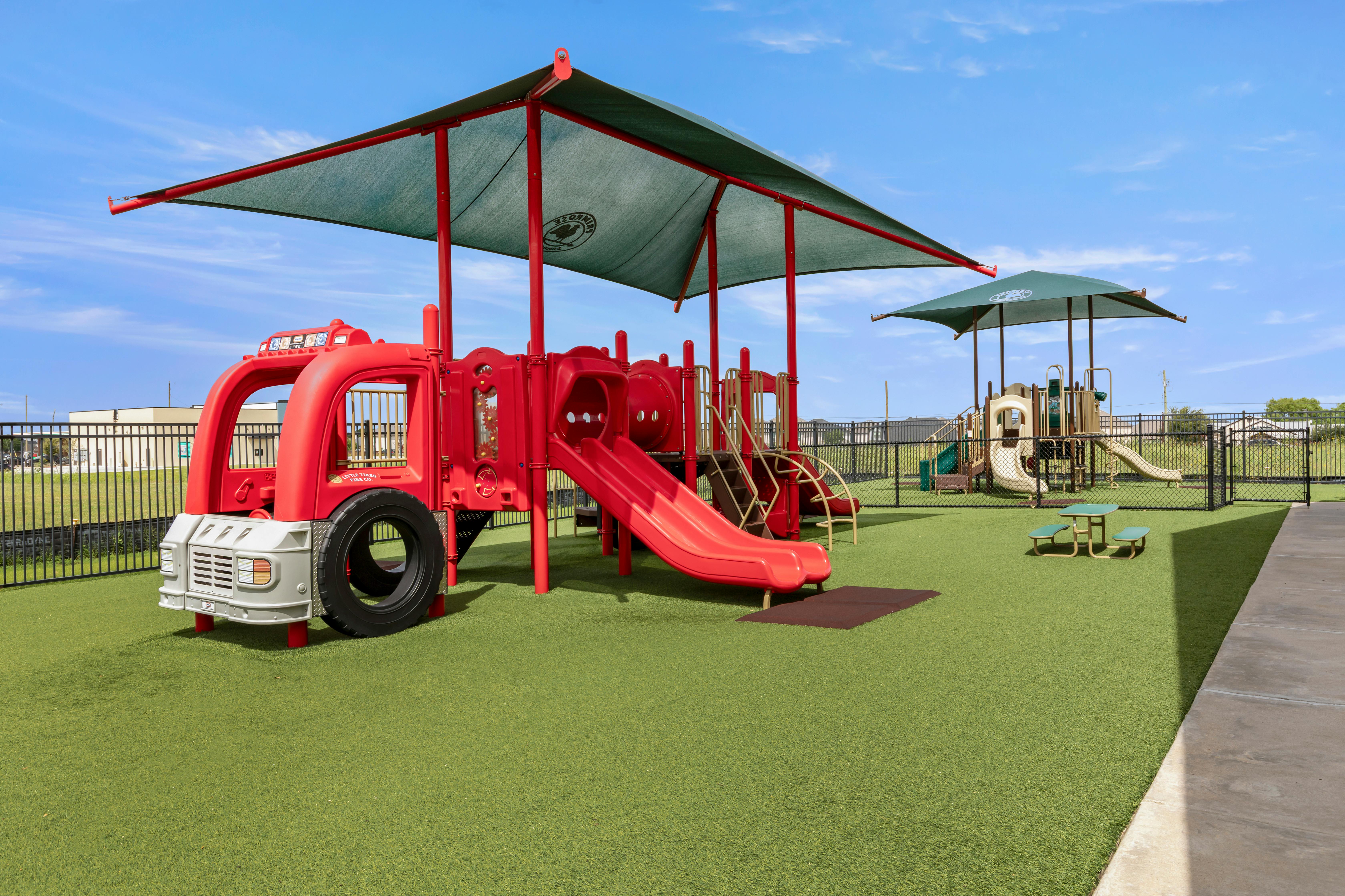 Playground with a red fire truck play structure and slides on green turf