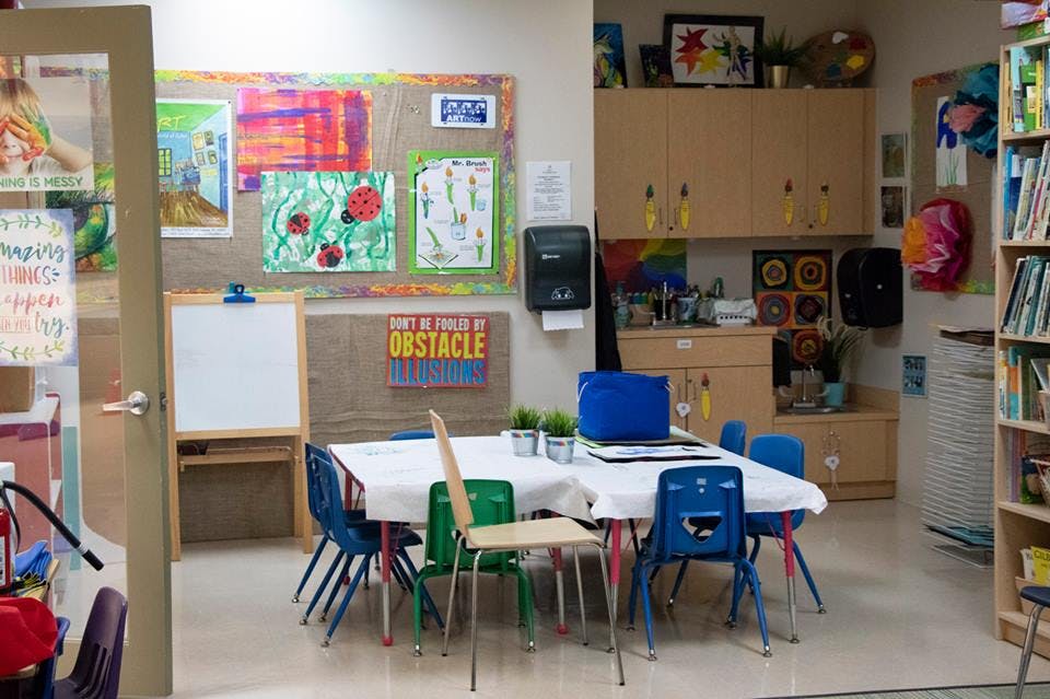 Classroom with a table and chairs, whiteboard, and colorful artwork on a bulletin board