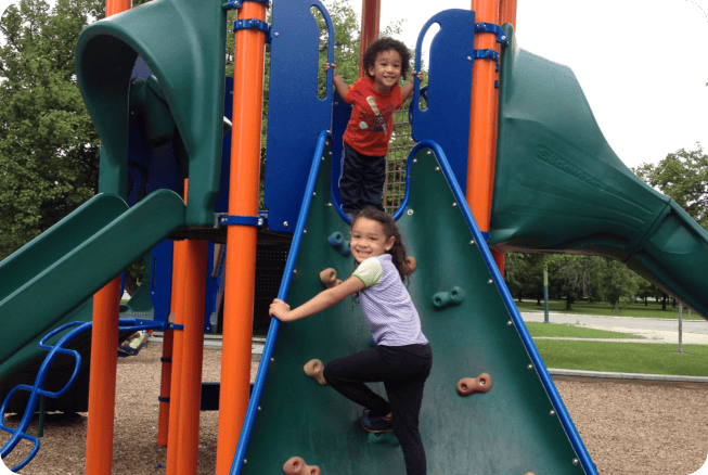 Two children on a playground structure, one climbing a rock wall, one at the top