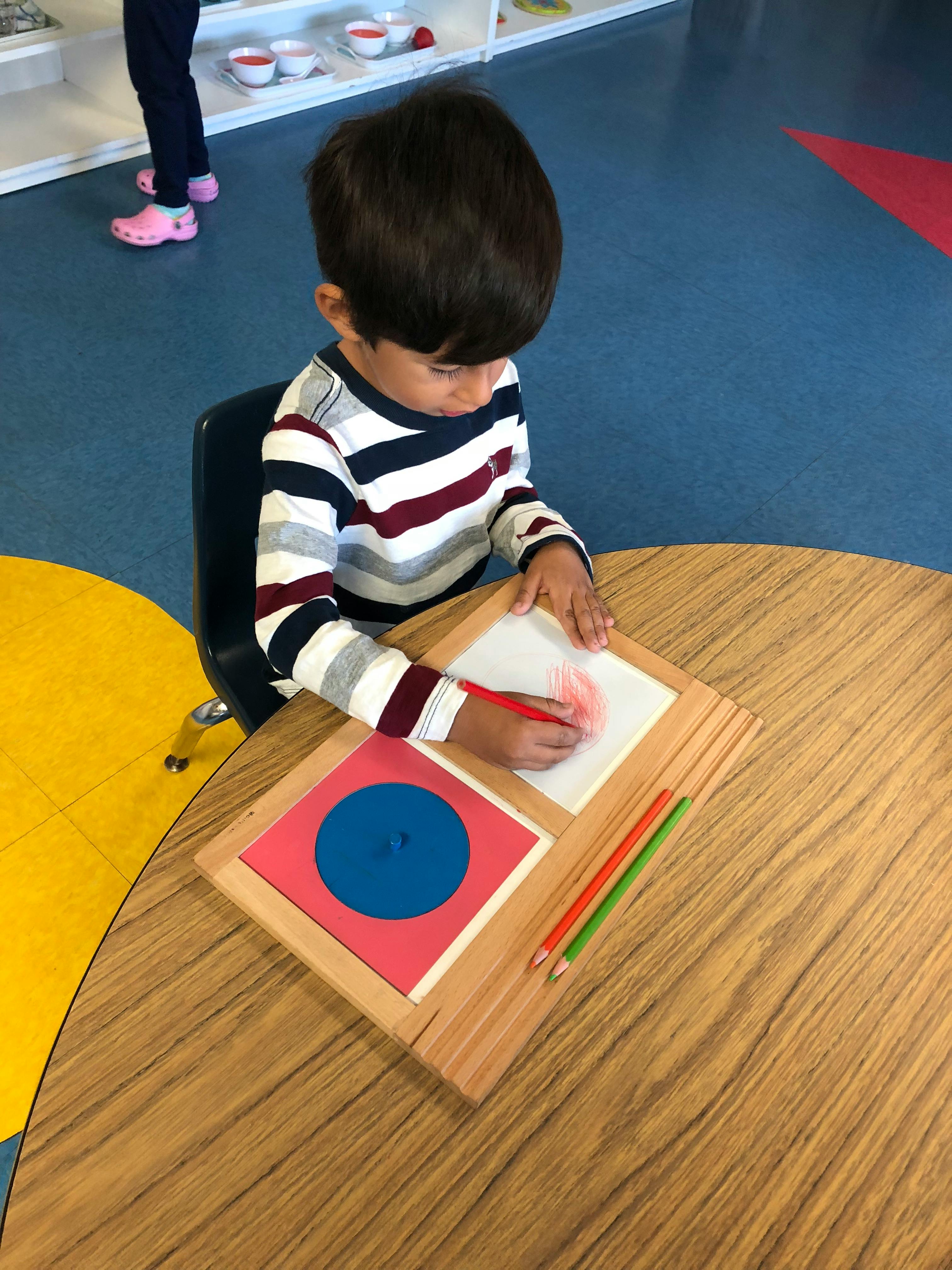 Child drawing on paper with a red pencil at a table