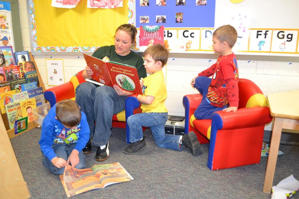 Adult reading a book to three children in a classroom