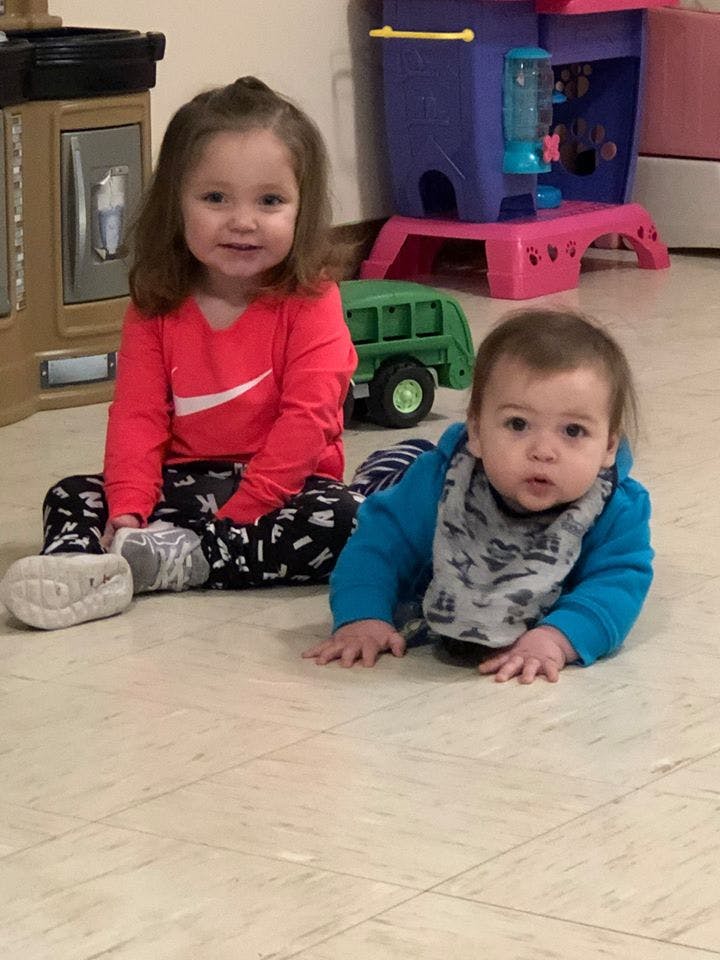 Child sitting on floor next to baby crawling
