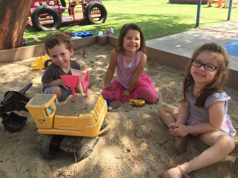 Three children playing in a sandbox with toys
