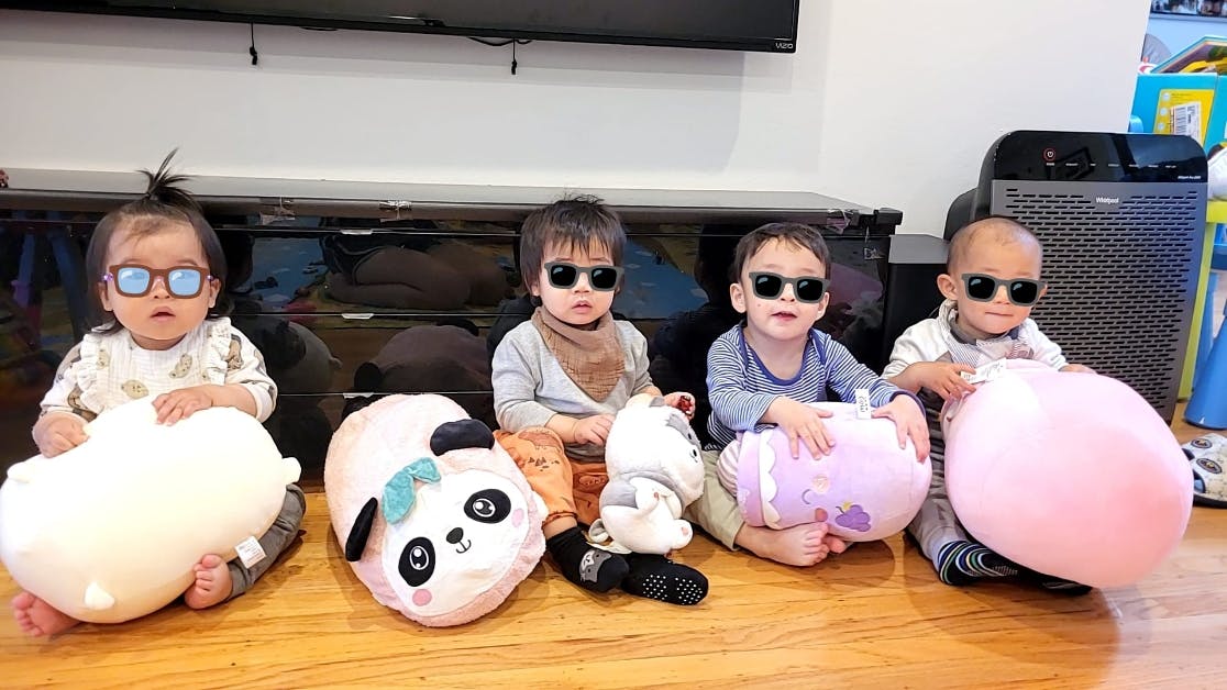 Four children sitting on a floor, three wearing sunglasses and one wearing glasses