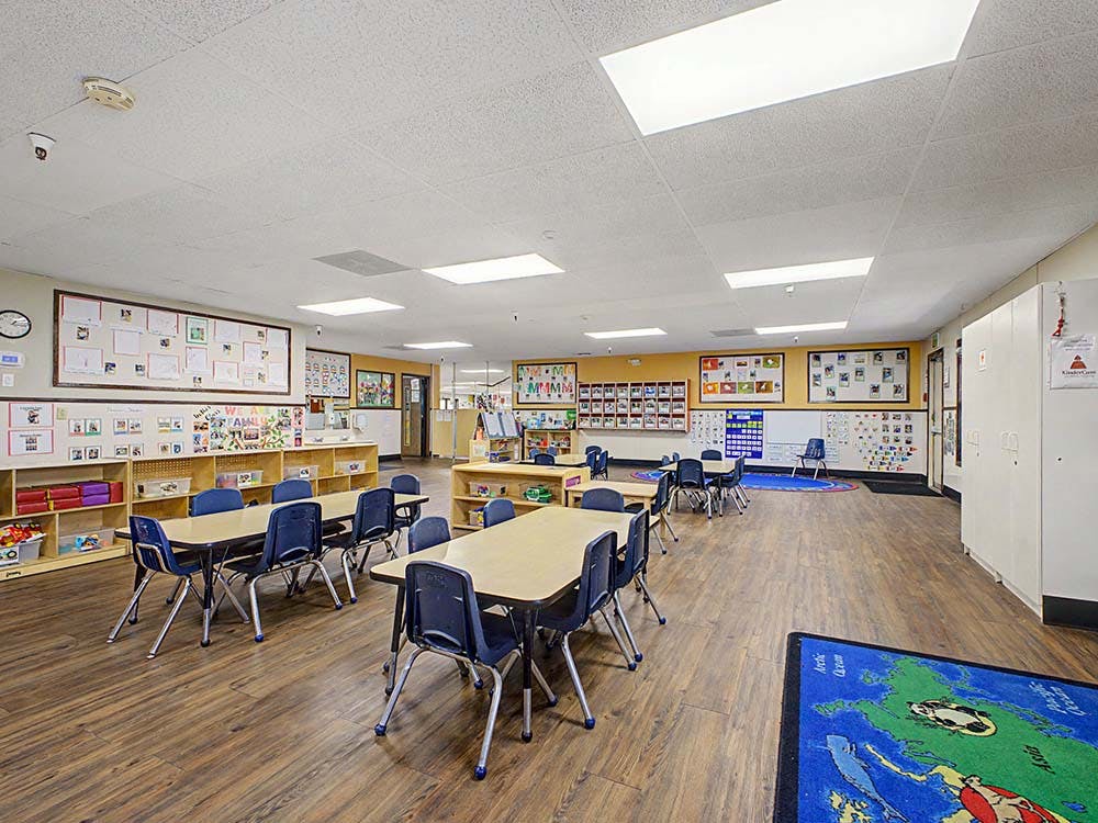 Empty classroom with small tables and chairs, shelves, and artwork on the walls