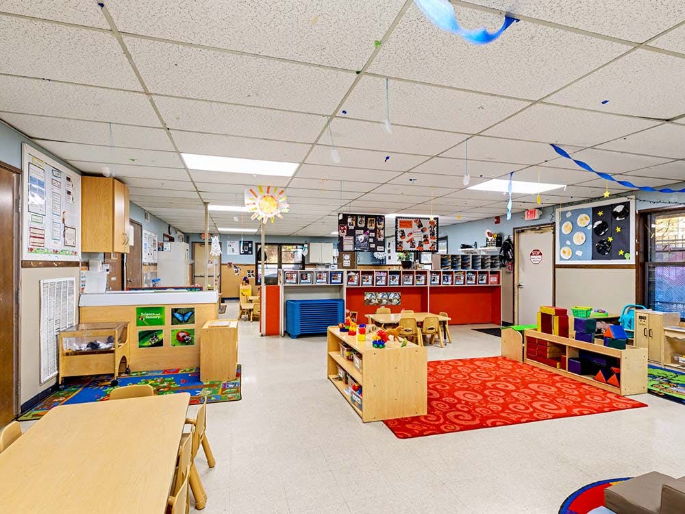 Empty classroom with small tables, chairs, and shelves with toys and supplies