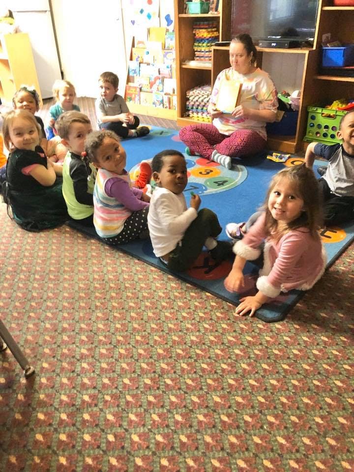 Adult reading to a group of children sitting on a rug in a classroom
