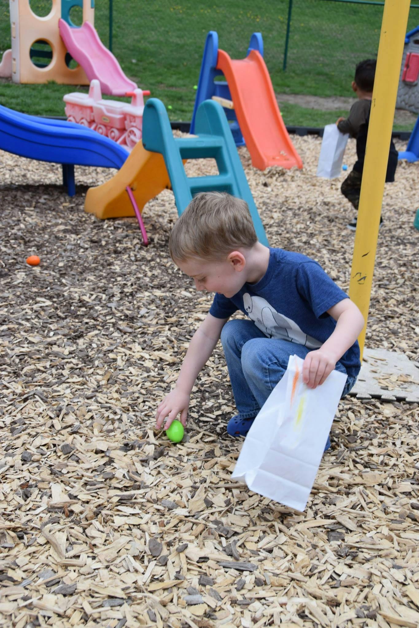 Child picking up an egg from wood chips on a playground