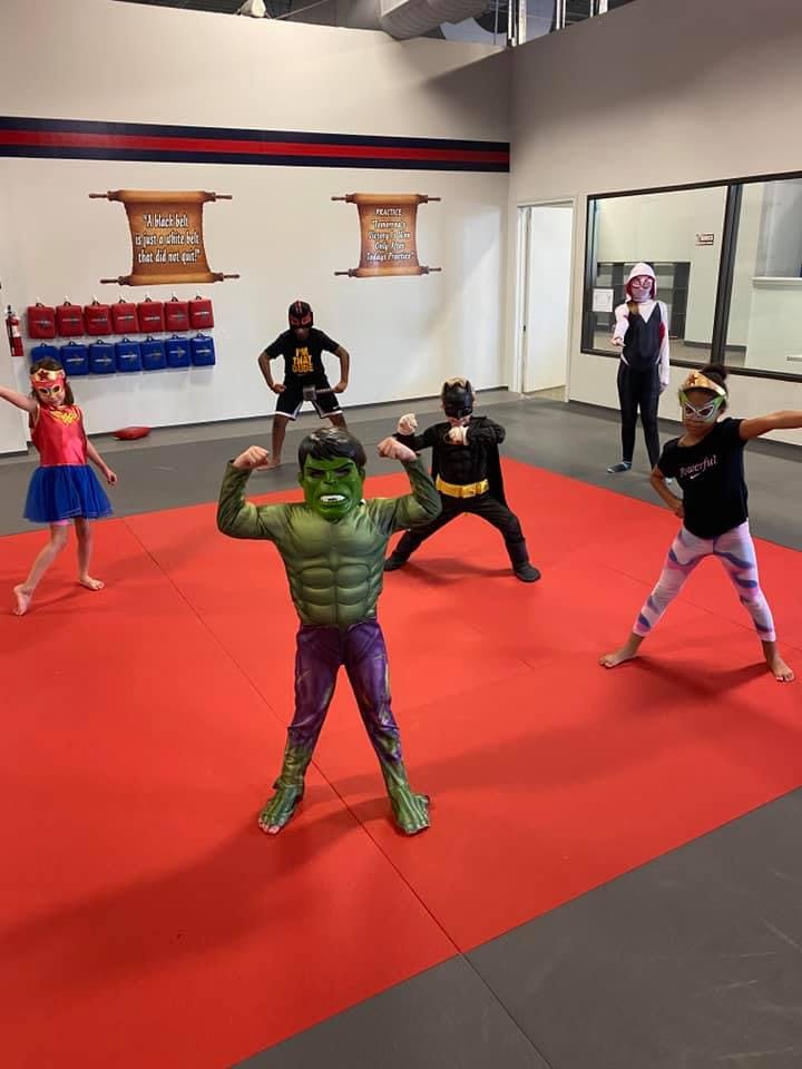 Children in superhero costumes posing on a red mat
