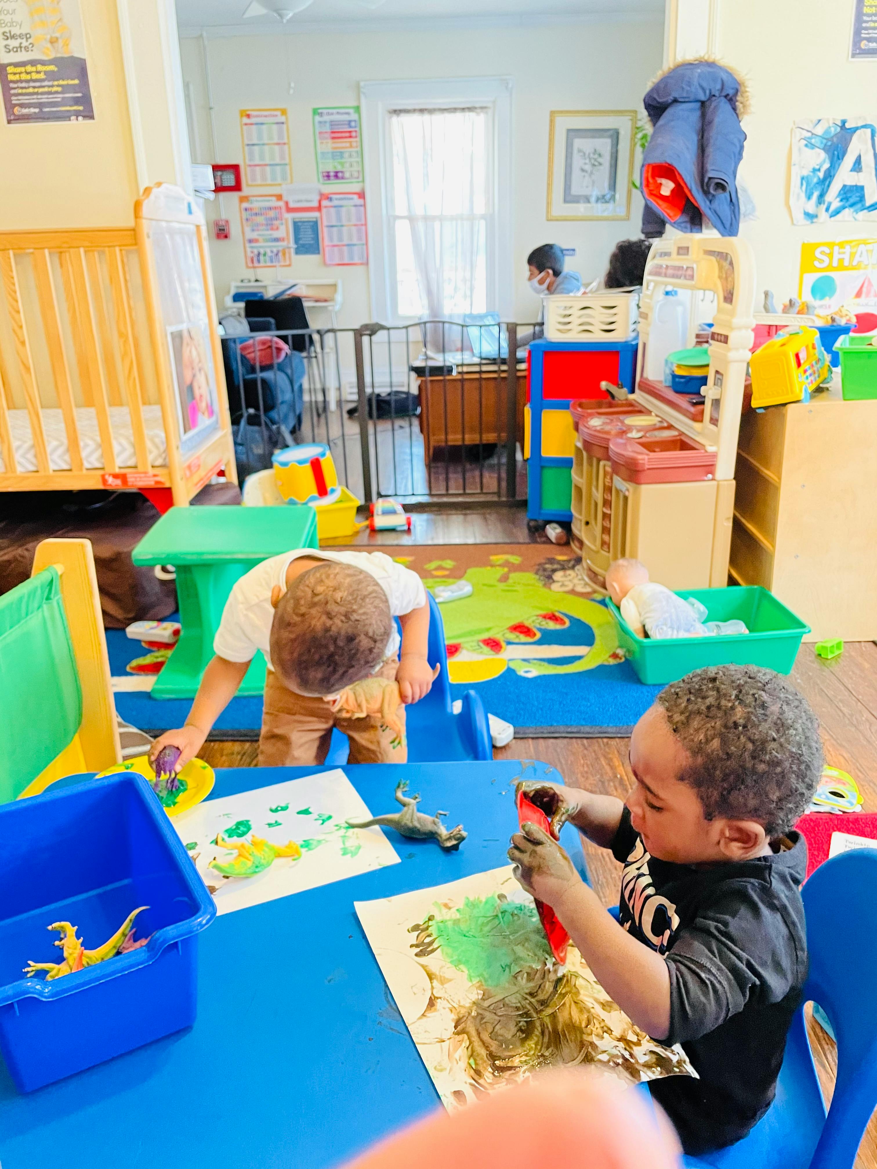 Two children painting at a blue table in a classroom