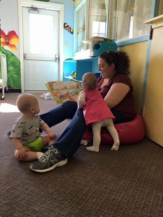 Person reading a book to two children on the floor