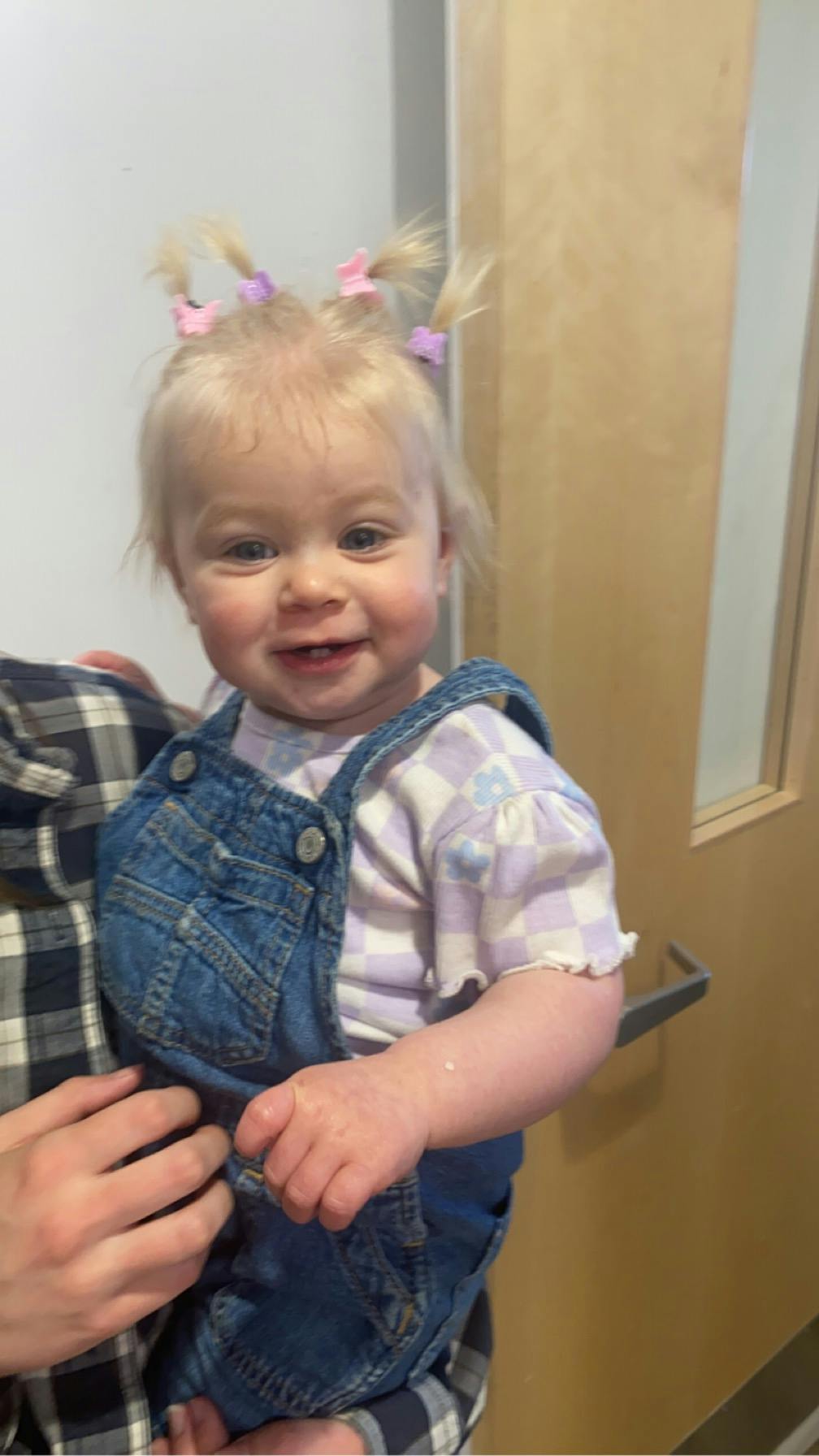 Child in denim overalls and checkered shirt being held