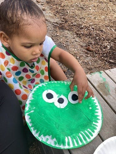 Child in a colorful bib making a craft with a green paper plate