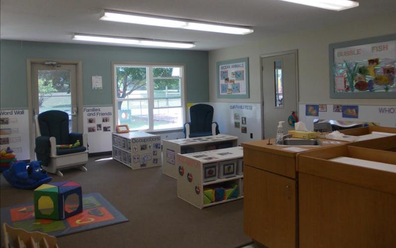 Children's classroom with chairs, storage units, educational posters, and a sink area