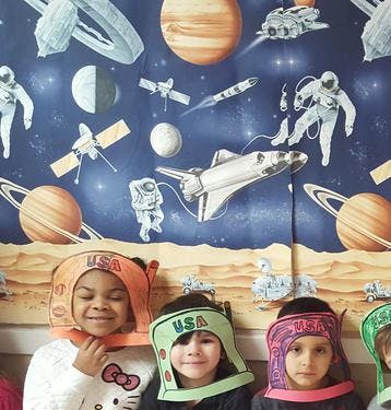 Three children wearing space-themed hats in front of a space mural