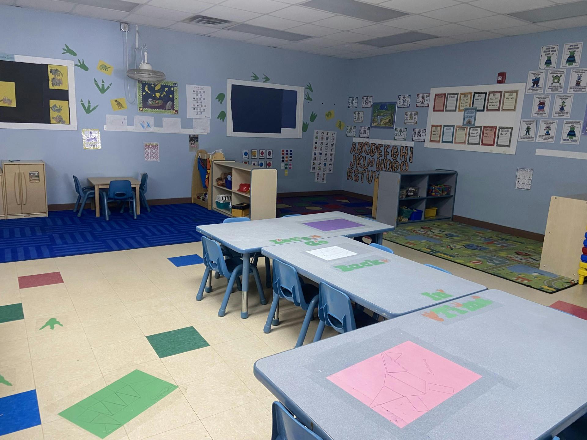 An empty classroom with small tables and chairs and colorful decorations on the walls
