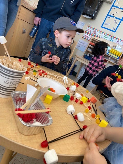 Child in a baseball cap making a structure with toothpicks and candy