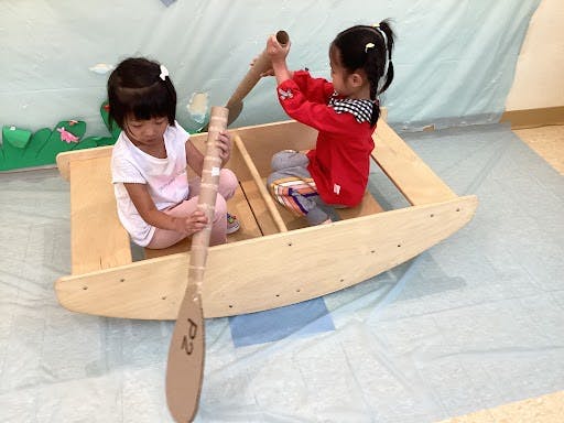 Two children playing in a wooden boat with paddles