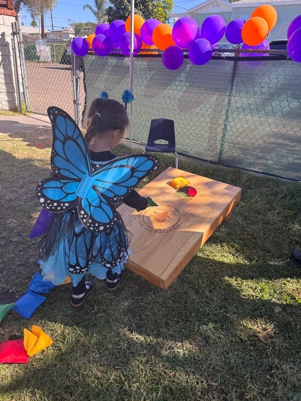 Child in butterfly costume playing cornhole