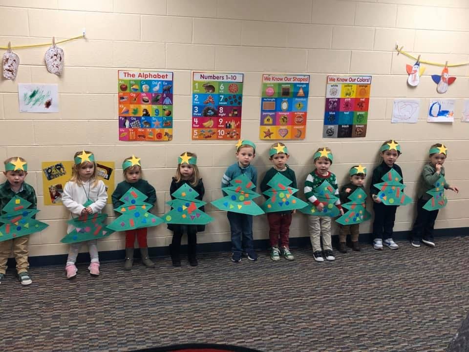 Children in a classroom wearing green Christmas tree costumes with star headbands