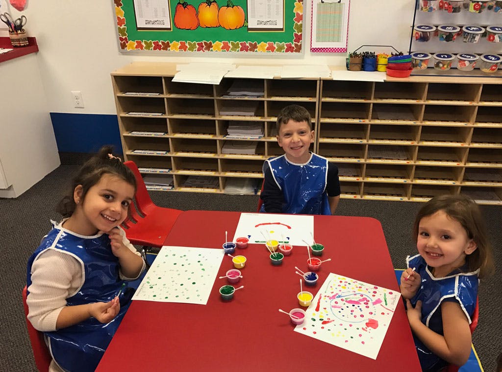 Three children painting at a red table in a classroom