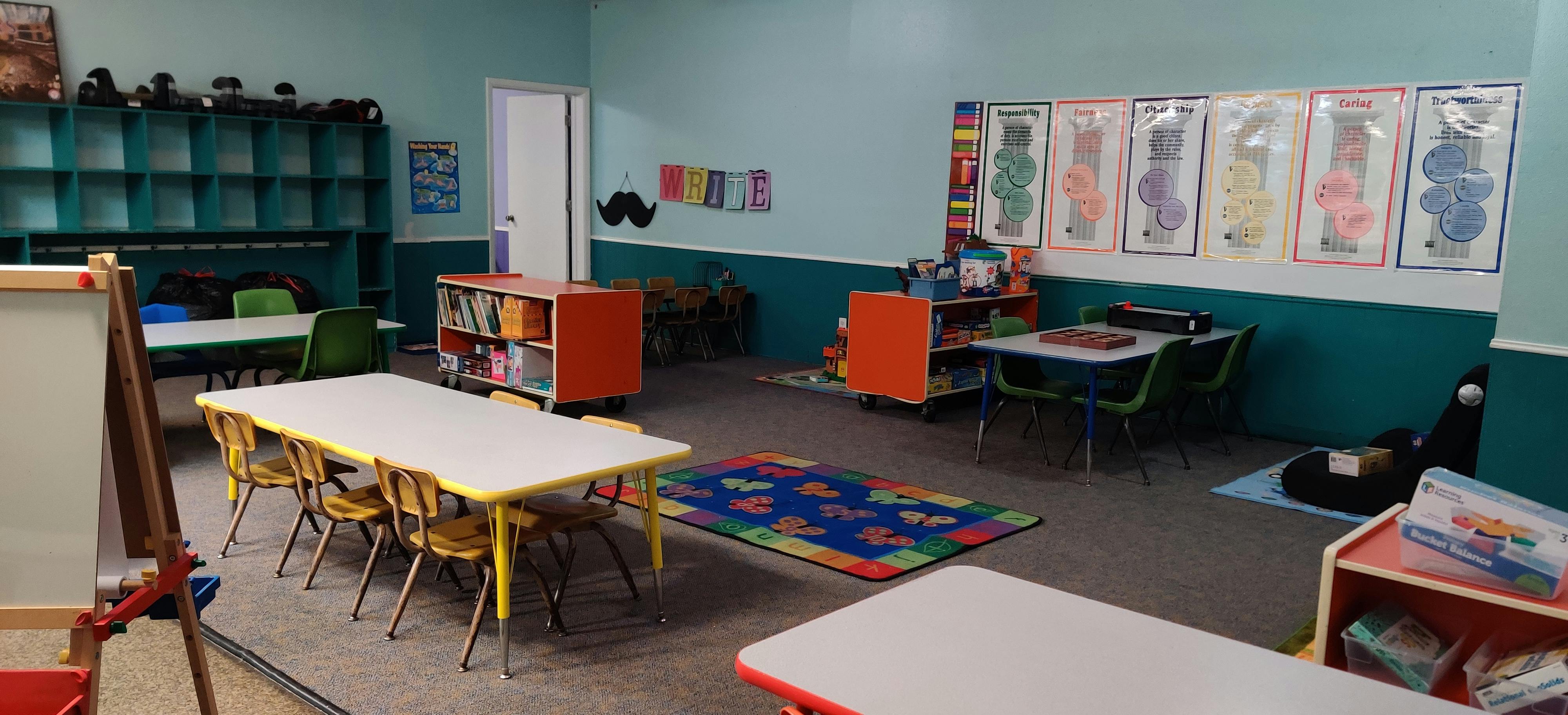 Classroom with small tables and chairs, shelves, and colorful rug