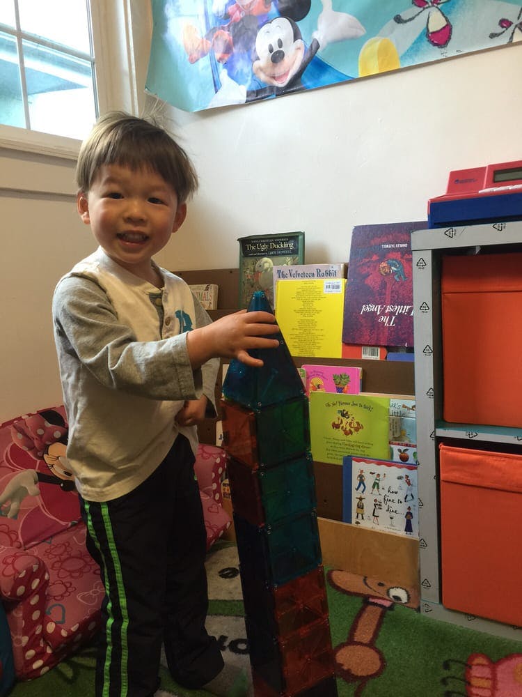 Child building a tower with colorful magnetic tiles in a room with books