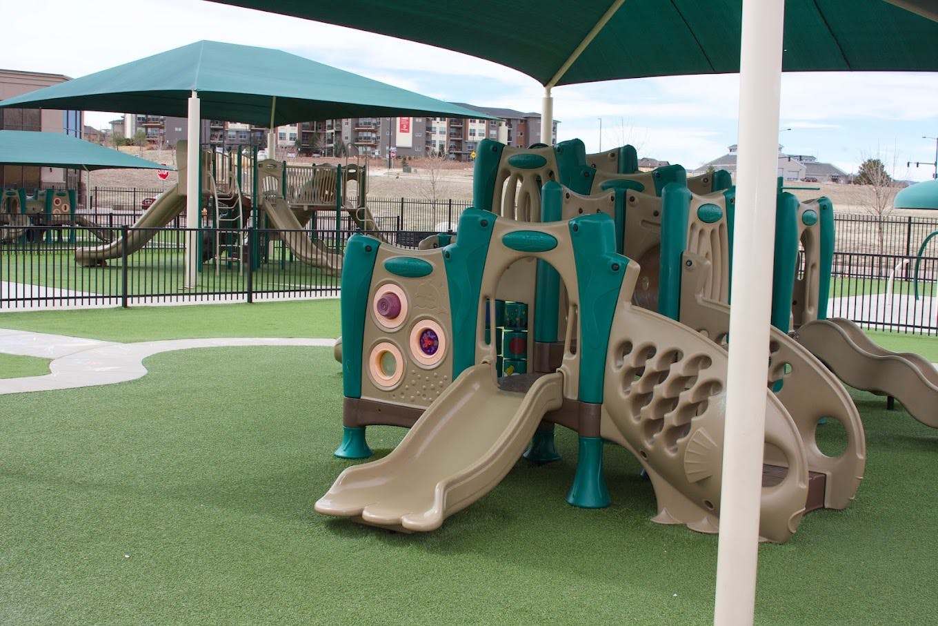Playground with multiple slides, climbers, and artificial grass under a large green canopy