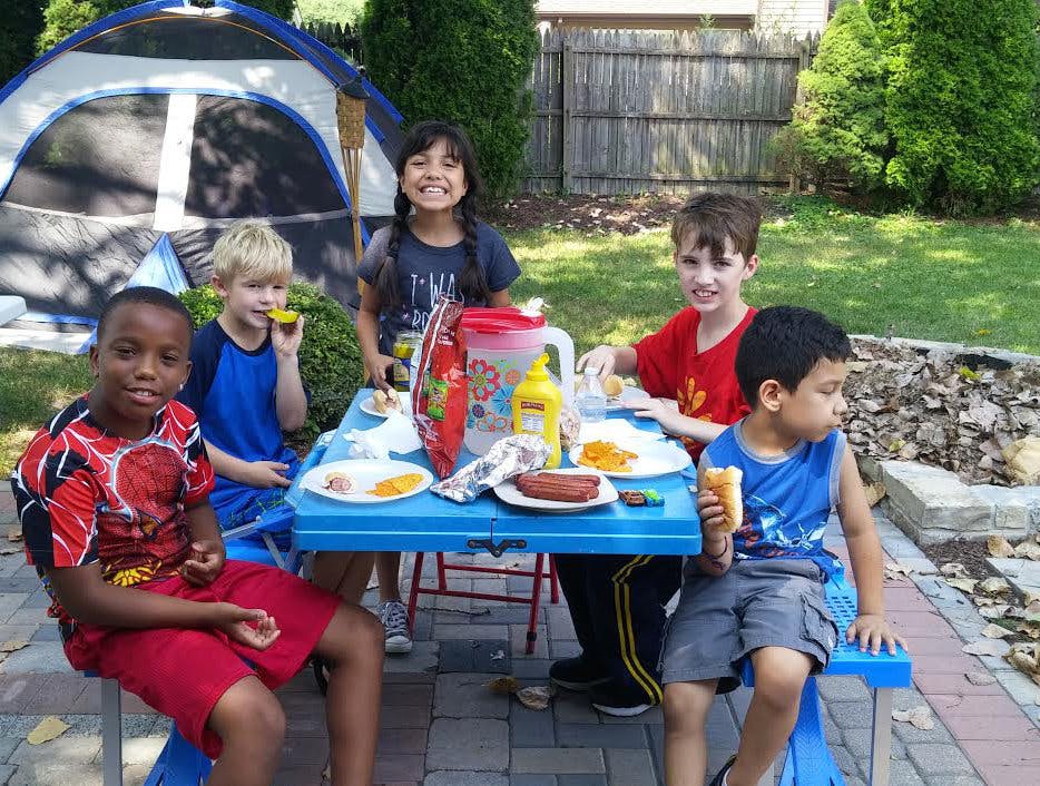 Children sitting around a blue picnic table with food
