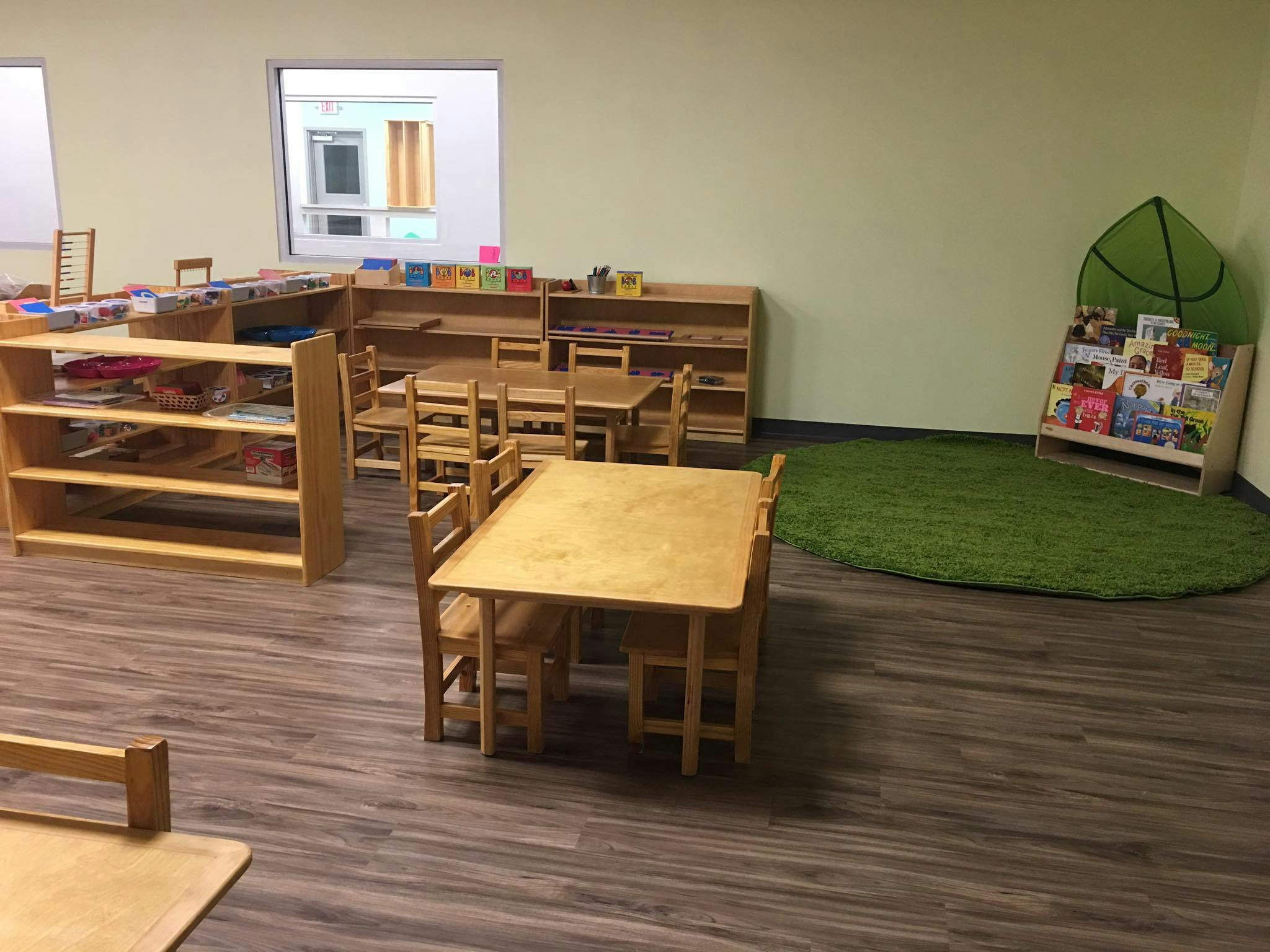 Classroom with wooden tables, chairs, shelves, and a green rug