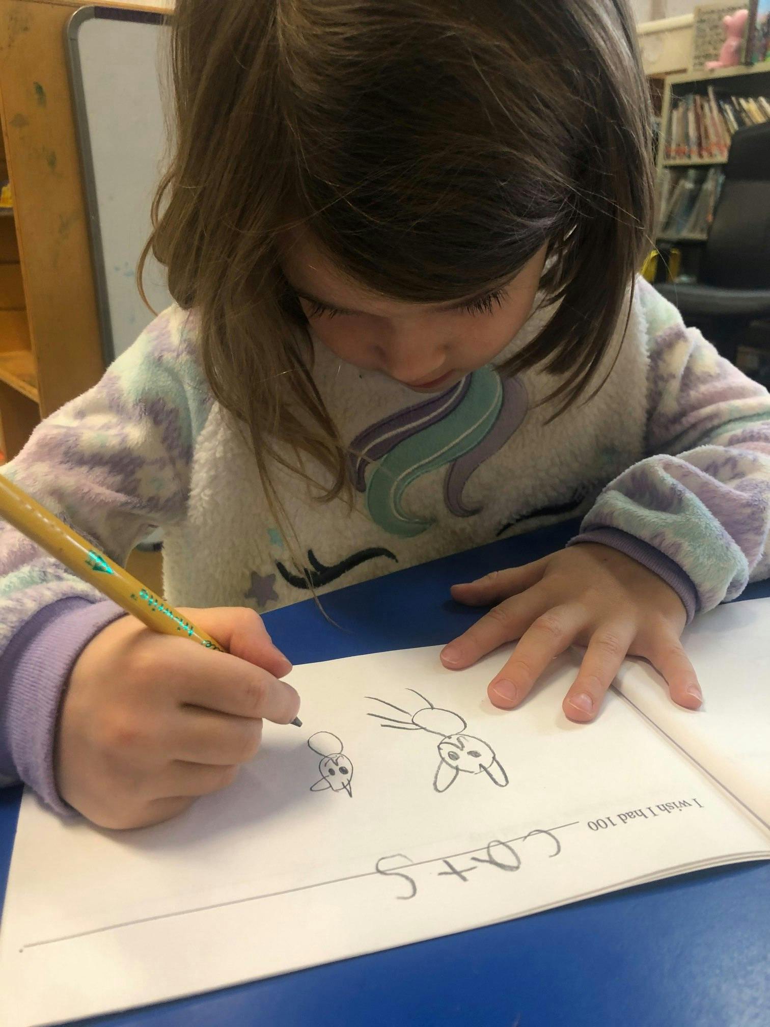 Child drawing cats on paper with a pencil on a piece of paper