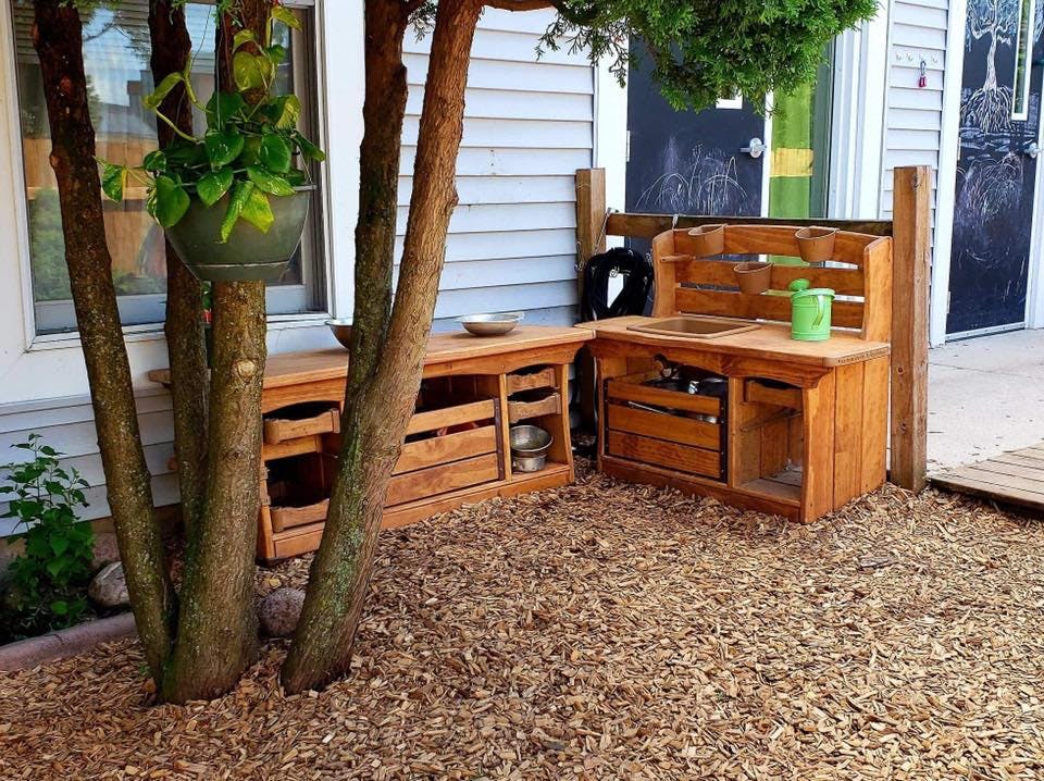 Outdoor wooden play kitchen and storage unit on wood chips