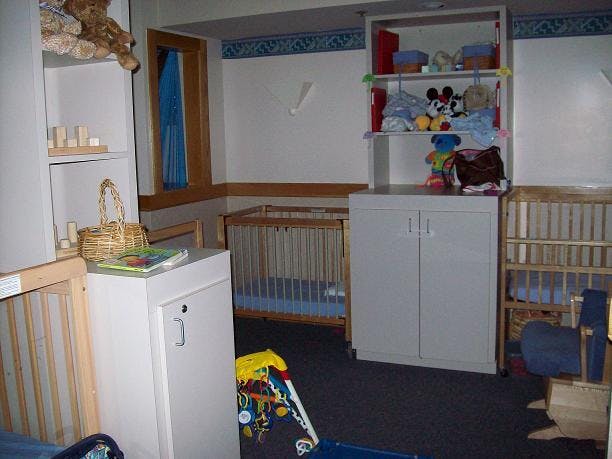 Room with multiple cribs and shelves with toys