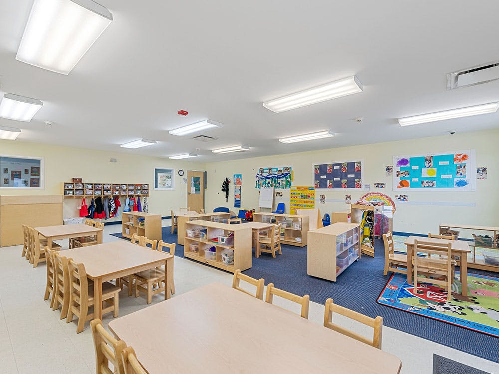 Classroom with small wooden tables, chairs, and cubbies
