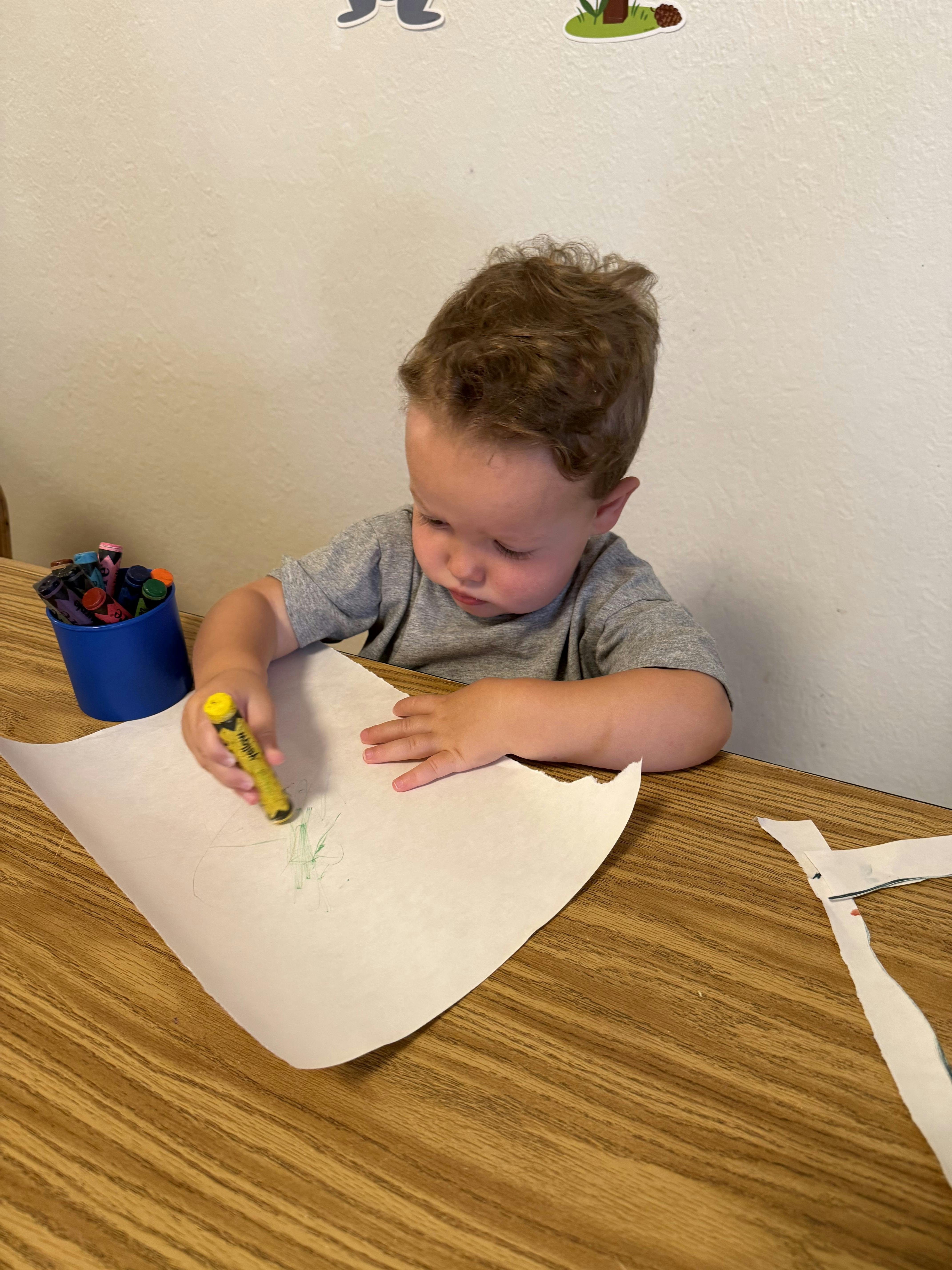 Child drawing on paper with a yellow crayon