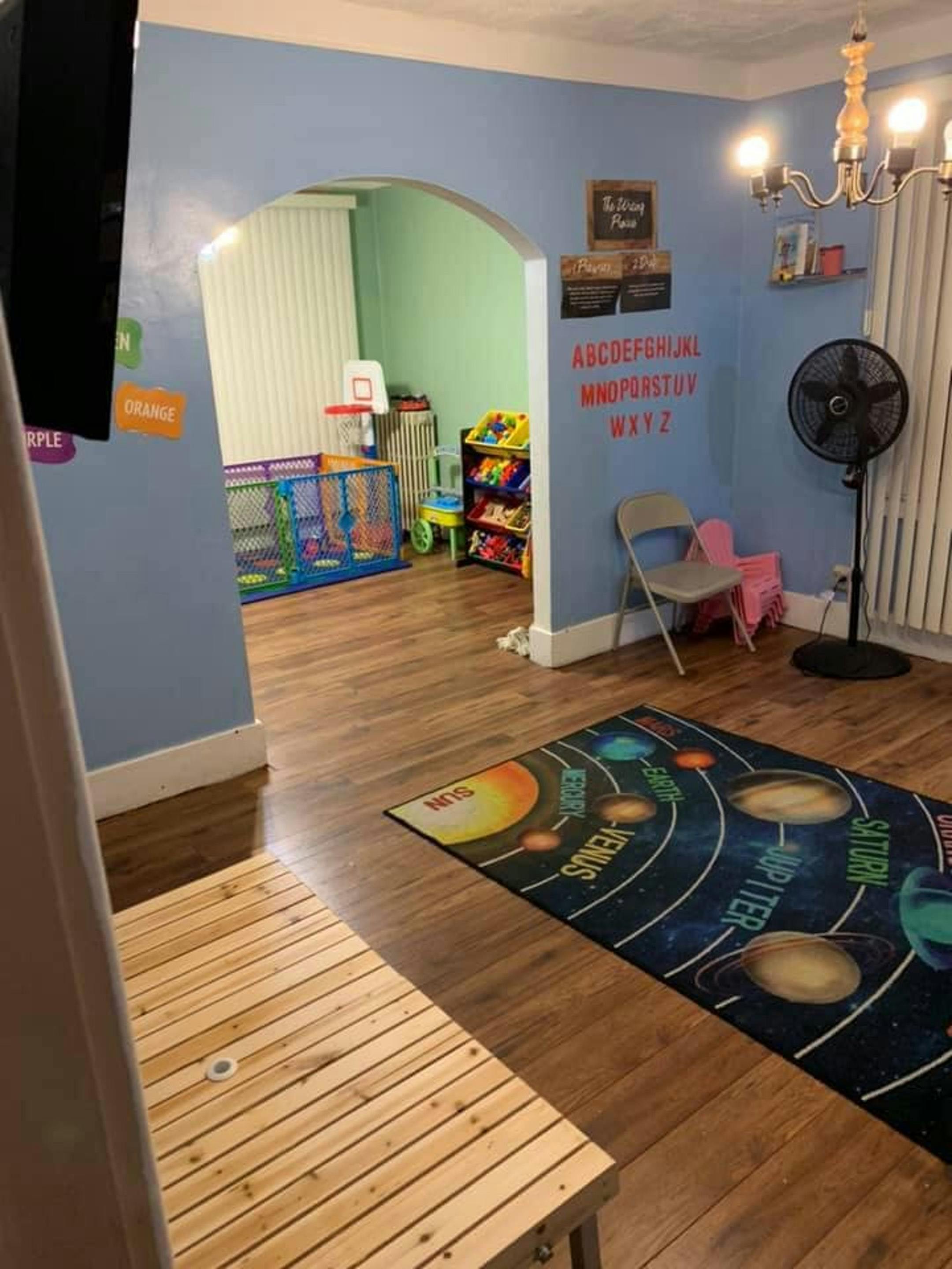 Room with a solar system rug, fan, and an arched doorway to another room with toys