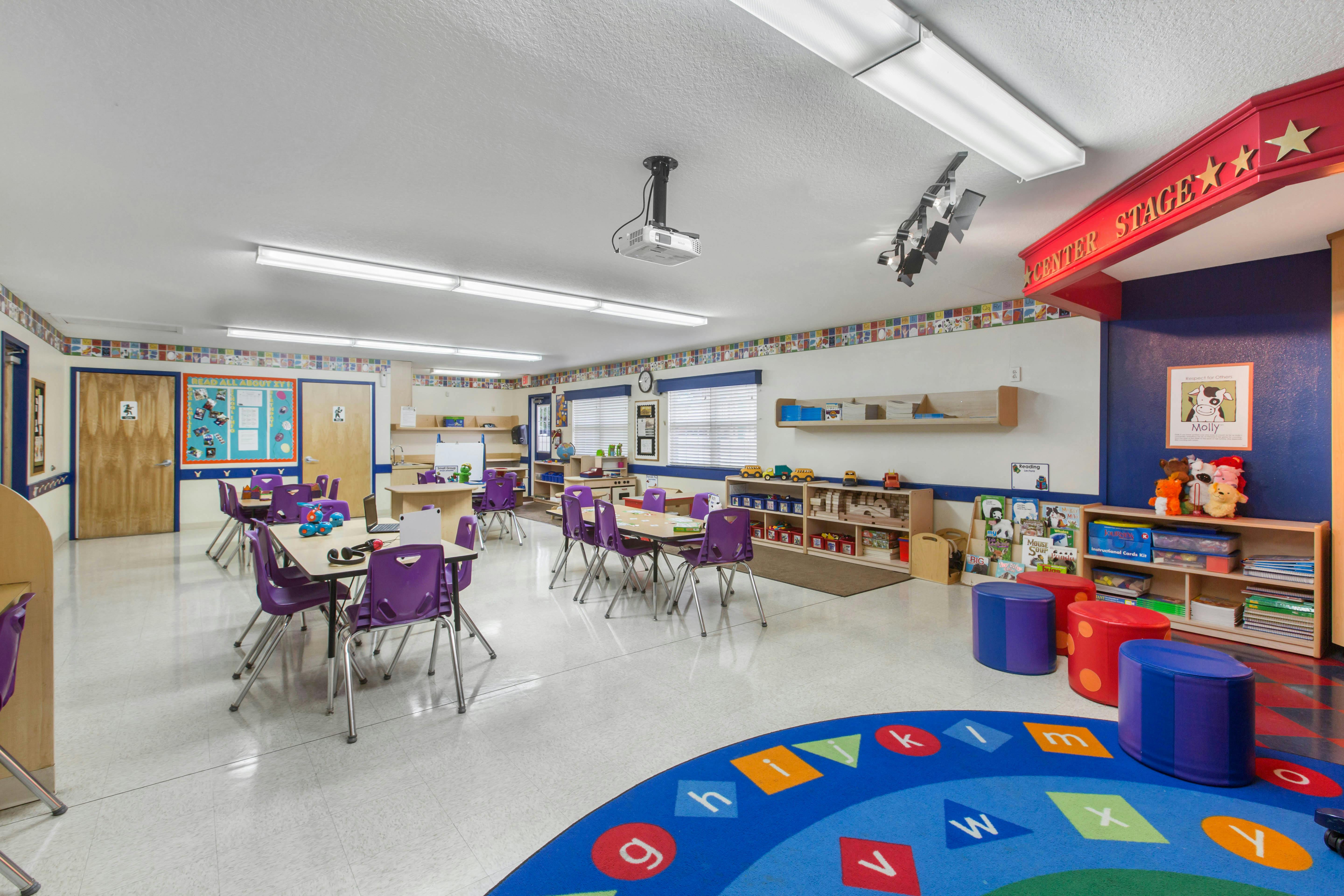Classroom with tables, purple chairs, toys, and a colorful alphabet rug