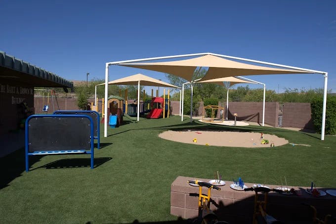 An outdoor playground with artificial turf, a sandbox, and play structures