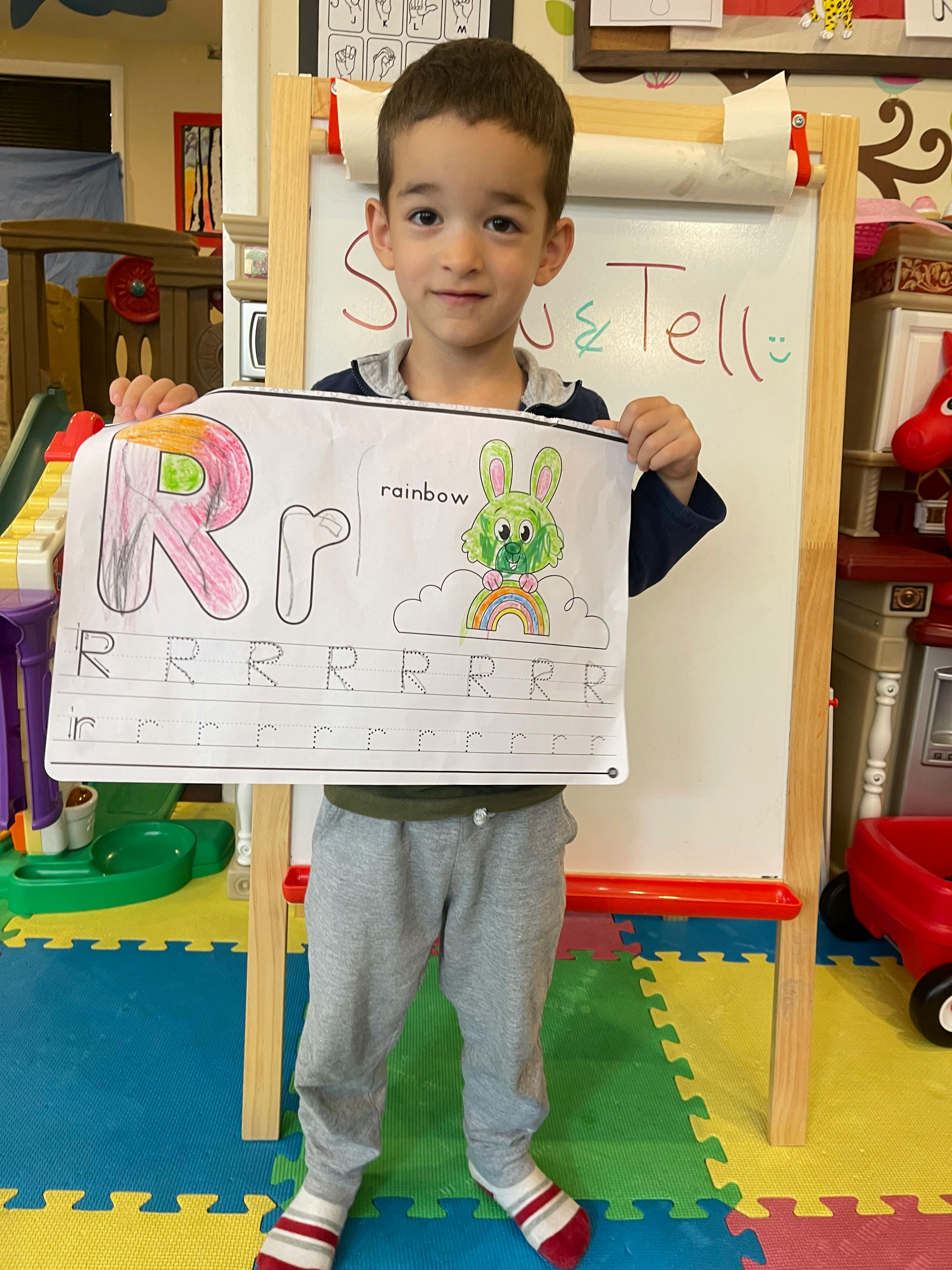 Child holding up a drawing of the letter R and a rabbit with a rainbow